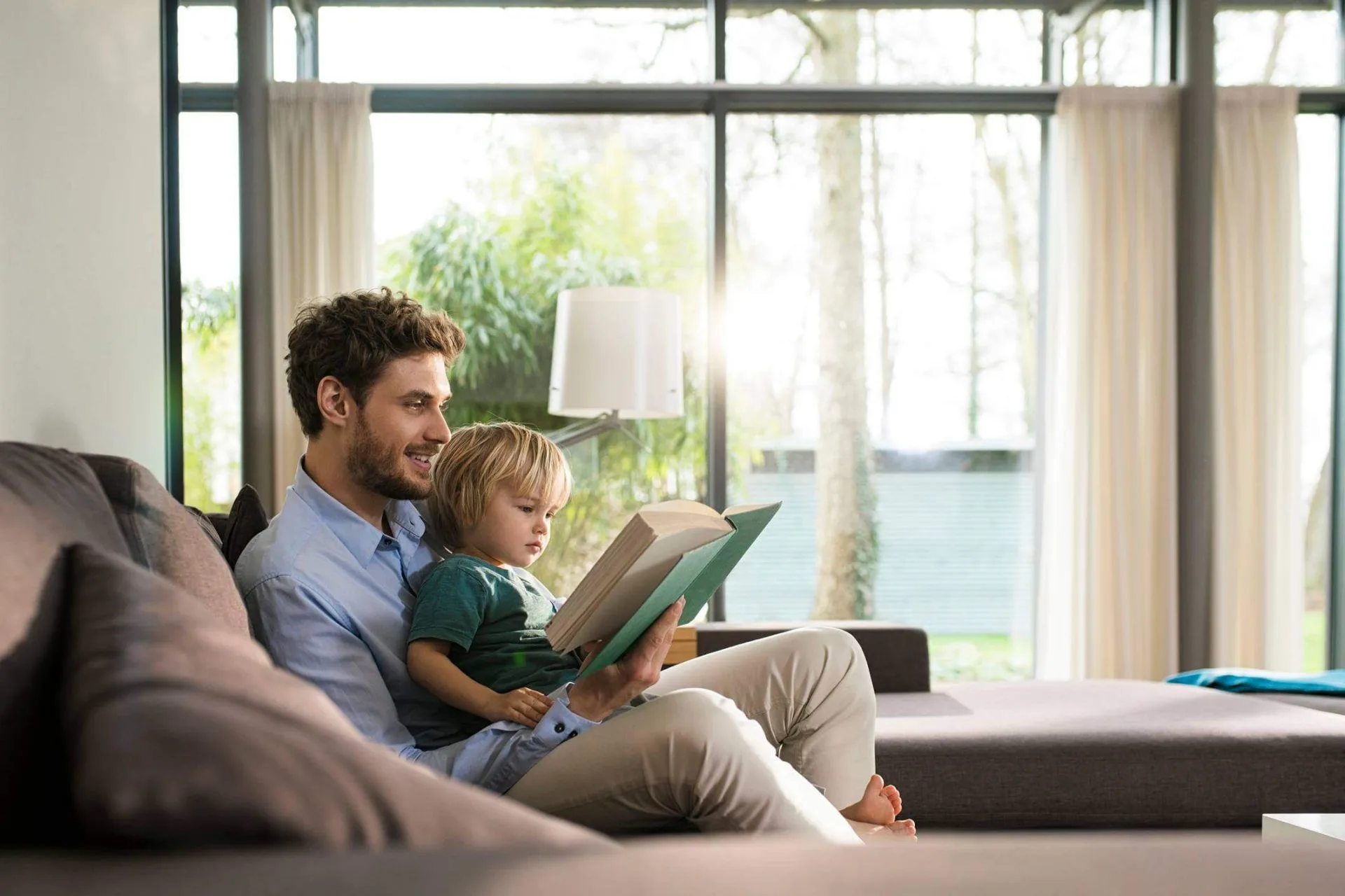 Un padre legge un libro con il figlio sul divano di casa